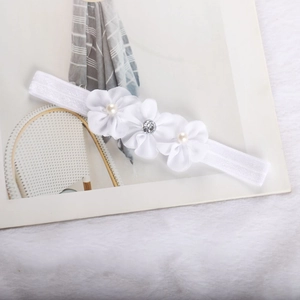 Close-up of white baby headband with three delicate fabric flowers and pearl accents