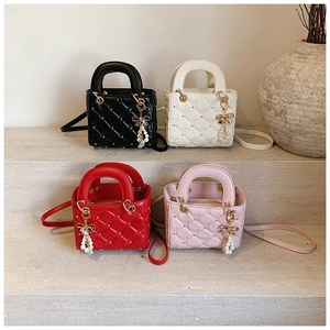Close-up of quilted pattern bags in four colors with pearl and bow charms on stone steps