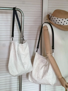 Close-up of beige embroidered cotton tote bags with elegant black leather straps and silver hooks