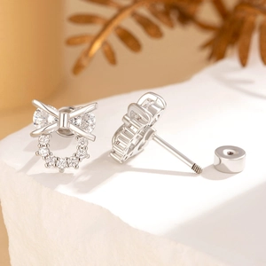 Elegant bow knot stud earrings with cubic zirconia stones on white textured pedestal