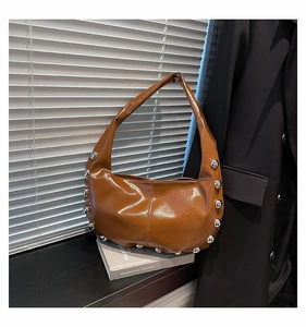 Detail of a brown crescent shoulder bag featuring stylish silver rivets and glossy leather