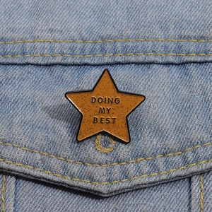 Macro view of star-shaped enamel badge with Doing My Best text on blue denim fabric
