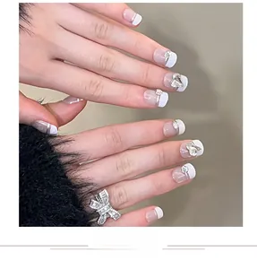Detail of French white tips nails with heart rhinestones and silver bow ring on hand