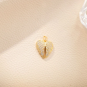 Detailed macro view of a gold leaf pendant with inlaid clear zircon on beige leather