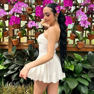 Side view of white tube pleated dress on model with blooming purple orchid background