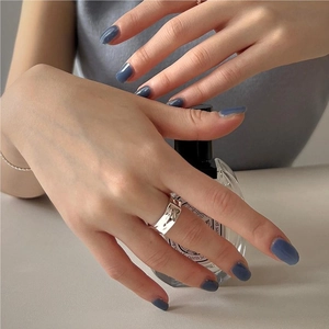 Macro shot of minimalist silver textured wide band ring on index finger with perfume bottle
