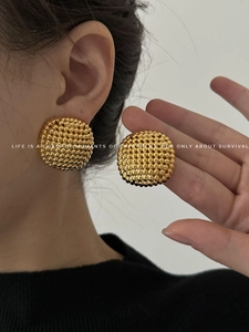 Detailed view of large gold hollow sphere earrings with intricate beaded metal texture