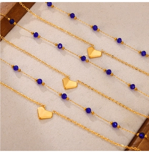 Detail of double layered gold heart necklace with dark blue beads on beige fabric