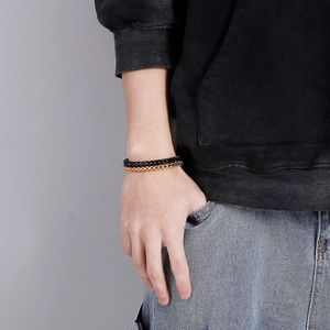 Detail of men's double-layered woven bracelets in black and gold on a wrist
