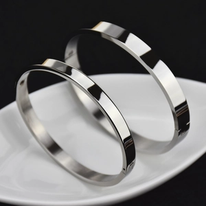 Polished silver stainless steel bangle bracelets set on white ceramic tray over black background