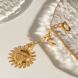 Golden stainless steel sun and moon pendants with facial engraving on textured glass tray