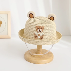 Close-up of beige straw hat featuring plush bear ears and detailed bear embroidery