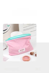 Pink fabric cosmetic bag with contrast green zipper shown with makeup tools