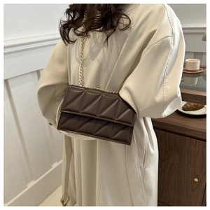 Detail of dark brown quilted leather crossbody bag with elegant gold chain strap on model
