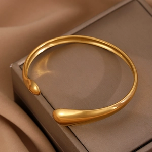 Macro view of polished gold teardrop cuff bracelet on a luxury silk and jewelry box base