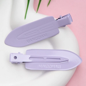 Close-up of two lavender purple matte metal hair clips on a white ceramic plate