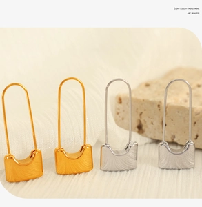 Macro detail of lock-shaped hook earrings in polished gold and silver metallic finish