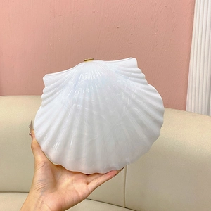 Detail of shell-shaped pearl white evening clutch with metallic clasp and iridescent finish