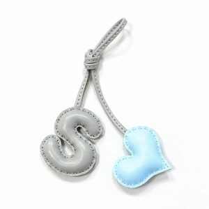 Detail of hand-stitched leather charm featuring a grey letter S and light blue heart shape