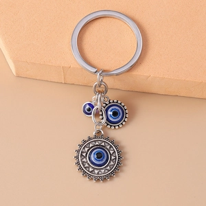 Close-up of silver metal keychain featuring blue evil eye and sun charms on a neutral base