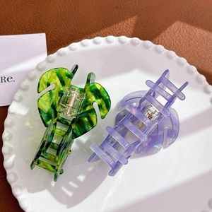 Leaf-shaped acetate hair claws in green and purple marble texture on a white plate