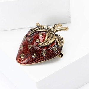Vintage enamel strawberry brooch with red finish and gold leaf details on white props