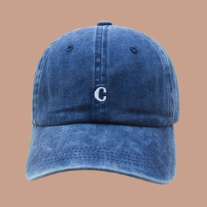 Detailed view of dark blue washed denim baseball cap with white embroidered C letter logo