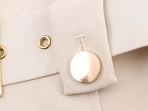 Makroaufnahme eines gold polierten Knopfes und einer Metallöse auf beigem Blazer-Stoff