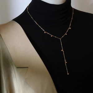 Close-up of Y-shaped gold bead tassel necklace on a black turtleneck sweater and suit