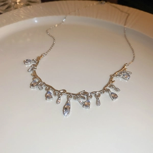 Silver branch necklace with sparkling teardrop gems on a minimalist white tray
