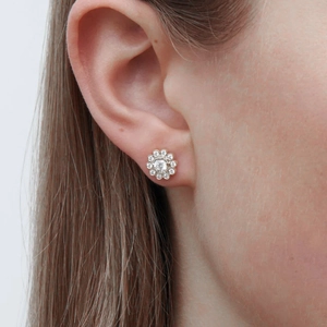 Detailed close-up of a silver flower stud earring featuring cubic zirconia on a model ear
