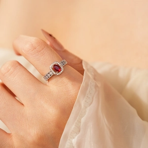 Close-up of elegant silver ring with oval red gemstone and pavé diamonds on a model