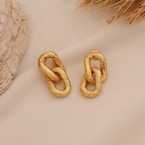 Detail of gold textured chain link earrings on a beige fabric background with a shell