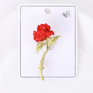 Detail of red rose brooch with green leaves on a white fashion jewelry card display