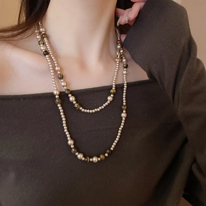 Dettaglio di una collana a strati con perle e occhio di tigre su collo e spalla della modella