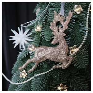 Detail of glitter champagne reindeer ornament hanging on a Christmas tree with warm lights