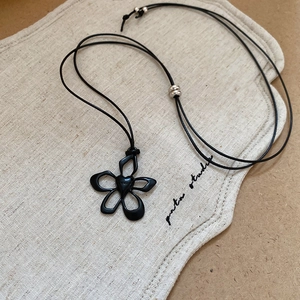 Detail of flower pendant necklace with heart center on black cord over a linen bag