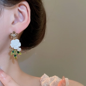Close-up of floral earring with white rose, green leaf and pearl on model's ear