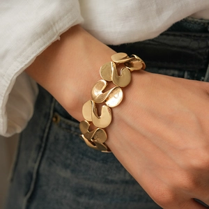 Detail shot of wide gold metallic S-curve linked bracelet on model with white shirt