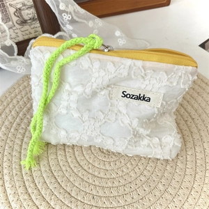 Détail du sac en dentelle crochetée blanche avec zip jaune et cordon vert néon sur paille