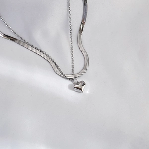 Detail of silver double-layered necklace with snake chain and heart pendant on silk
