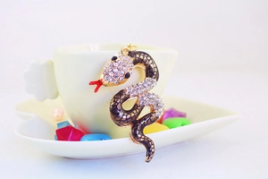 Macro detail of a golden snake pendant with white crystals and red enamel tongue