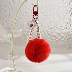 Détail du porte-clés pompon rouge avec chaîne de perles et charme fleur en cœur