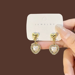 Macro detail of gold-plated heart-shaped pearl earrings with sparkling rhinestone halo