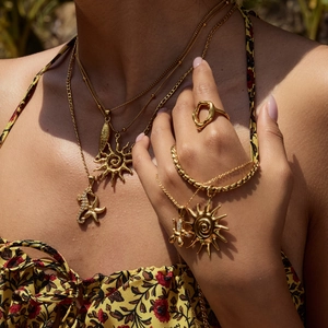 Close-up of layered gold necklaces and rings on model in a tropical outdoor setting