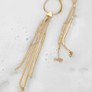 Elegant gold triangle fringe necklace with multilayered snake chains over foam and water