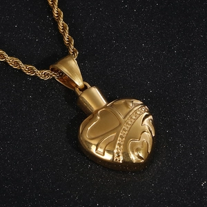 Macro shot of gold heart urn pendant with rope chain on black glitter background
