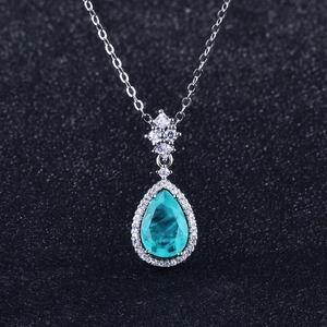 Luxurious pear-cut teal gemstone necklace with halo diamonds on a black textured backdrop
