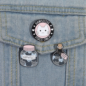 Detailed view of three cat enamel pins with motivational quotes on denim fabric