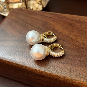 Macro shot of gold plated zircon hoop earrings with large white drop pearls